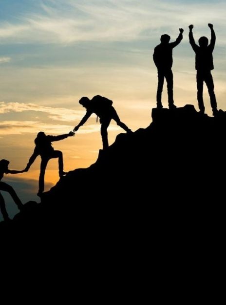 people in silhouette climb a mountain, helping eachother up and celebrating at the top