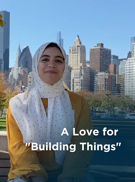 A woman in a yellow shirt and white hijab smiles in front of the New York City skyline