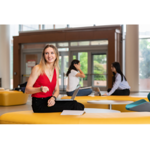 a woman in a red shirt sits in a sunny atrium